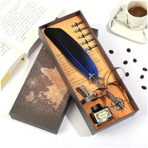Feather pen set with ink bottle and nibs in a decorative box on a table with coffee and books.